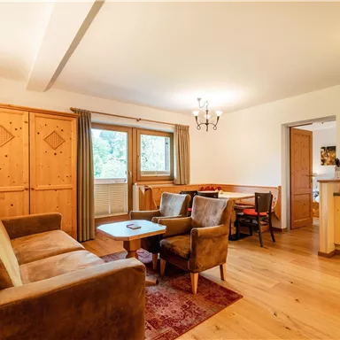 Gemütliches Wohnzimmer mit einem braunen Sofa und Holzdetails. Große Fenster sorgen für viel Tageslicht und eine einladende Atmosphäre.