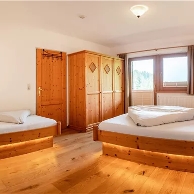 Ein gemütliches Schlafzimmer mit zwei Einzelbetten aus Holz. Es gibt einen großen Kleiderschrank und ein Fenster mit Blick nach draußen.
