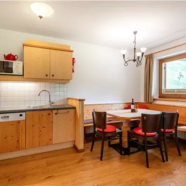 Eine gemütliche Küche mit Holzschränken und einem Essbereich. Ein Tisch mit Stühlen und eine Fensterbank, die Tageslicht hereinlässt.