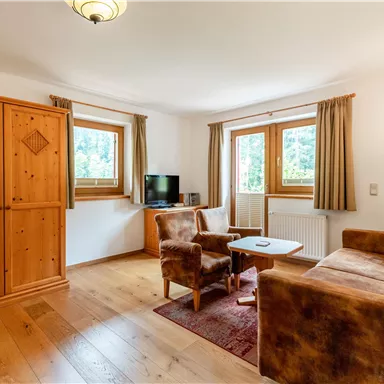 Ein gemütliches Wohnzimmer mit einem Holzschrank und einem Sofa. Große Fenster lassen viel Licht herein und bieten einen schönen Blick nach draußen.