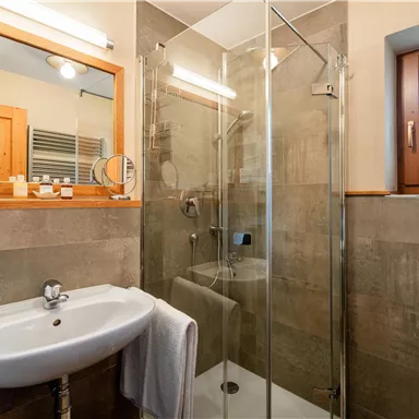 Ein modernes Bad mit einer Glasdusche und einem Waschbecken. Die Wände sind in neutralen Farben gehalten und ein Fenster bietet Tageslicht.