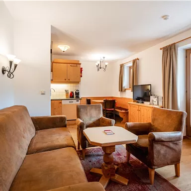 Ein gemütliches Wohnzimmer mit einer Couch und zwei Stühlen. Die offene Küche ist gut ausgestattet und es gibt ein Fenster mit Blick nach draußen.