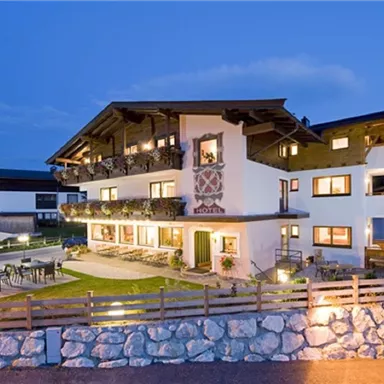 A charming hotel in alpine style, illuminated at dusk.
Surrounded by green lawn and an inviting terrace.