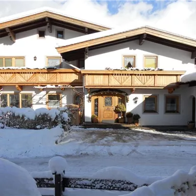 A beautiful house in alpine style, surrounded by snow. The sky is clear and the sun is shining.