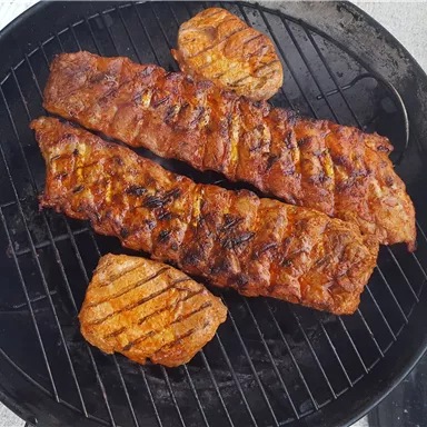 Gegrillte Rippchen und Steak auf einem Grill. Das Fleisch hat eine appetitliche, goldbraune Farbe.