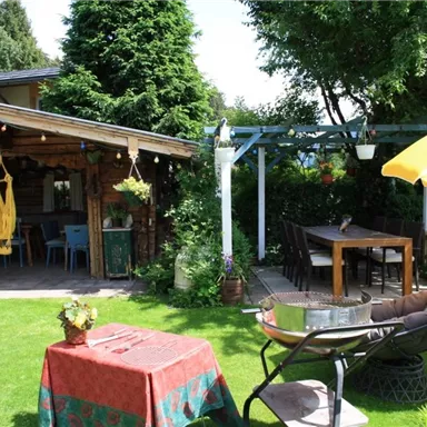 Ein einladender Garten mit einer romantischen Holzhütte. Es gibt einen Tisch, Stühle und einen sonnigen Sonnenschirm.