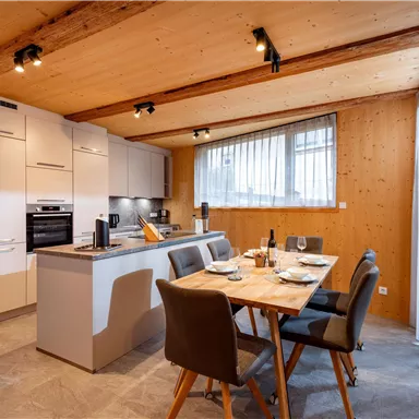 Modern kitchen with dining area, wooden cladding, and large windows. The table is set and creates an inviting atmosphere.