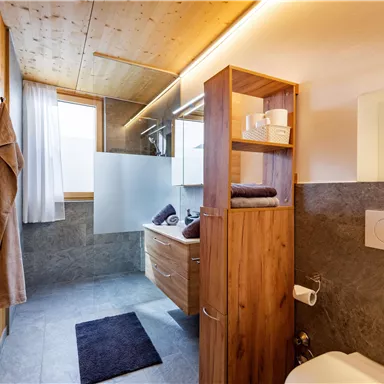 A modern bathroom with wooden and stone accents. It features a shower, a wash area, and ample natural light.