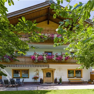 Ein gemütliches Haus mit Balkonen, die mit bunten Blumen geschmückt sind. Der Garten ist grün und einladend, ideal für Entspannung im Freien.