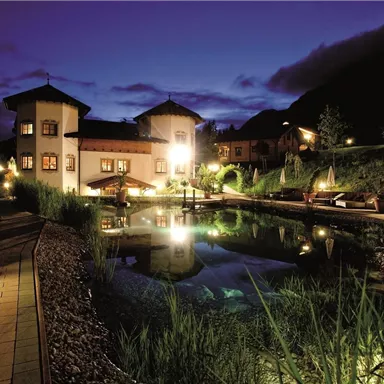 Ein malerisches Hotel mit einem ruhigen Teich im Vordergrund. Die Umgebung ist sanft beleuchtet und vermittelt eine gemütliche Atmosphäre in der Dämmerung.