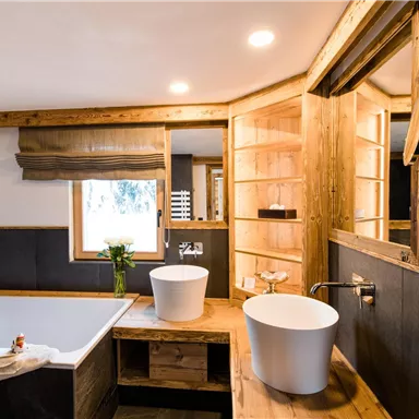 Ein modernes Badezimmer mit einer freistehenden Badewanne und einem Waschbecken aus Weiß. Holz- und Steinakzente schaffen eine elegante Atmosphäre.