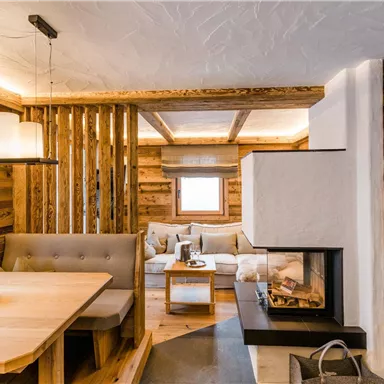 Ein gemütlicher Wohnraum mit einer Holzdecke und einem modernen Kamin. Der Raum ist hell und einladend, mit einem großen Esstisch und einer bequemen Sitzecke.