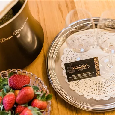Ein elegantes Arrangement mit einer Champagnerkühlbox, zwei Weingläsern auf einem silbernen Tablett und einer Schale frischer Erdbeeren. Dazu liegt eine Karte mit dem Namen "Dom Pérignon".