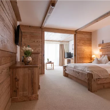 Ein modernes Zimmer mit rustikalem Holzinterieur und einem komfortablen Doppelbett. Große Fenster sorgen für viel Tageslicht und einen einladenden Raum.