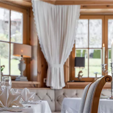 Ein eleganter Speisesaal mit hübschen Fenstern und hellem Holz. Der Tisch ist schön gedeckt mit Blumen und Kerzen.