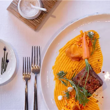 Ein kunstvoll angerichteter Teller mit zartem Fleisch und püriertem Gemüse. Dazu sind frische Kräuter und dekoratives Gemüse platziert.