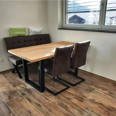 Ein modernes Esszimmer mit einem Holztablett und bequemen Stühlen. Große Fenster bieten viel Tageslicht und einen Blick nach draußen.