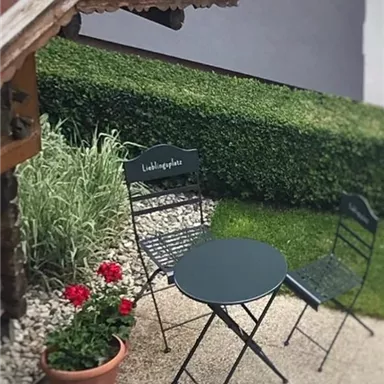 A small garden area with a round table and two chairs. Flowers and a well-maintained hedge complete the relaxed atmosphere.