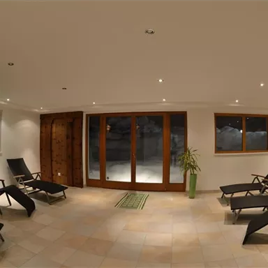 Ein entspannender Raum mit Liegen und großen Fenstern. Durch die Fenster ist eine ruhige Aussicht auf die Außenwelt zu sehen.