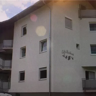 Ein mehrstöckiges Wohnhaus mit Balkonen und einer hellen Fassade. Das Gebäude trägt das Logo "Life-Residenz".