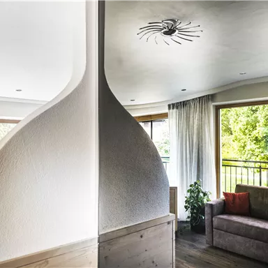 Ein modernes Wohnzimmer mit einem eleganten Raumteiler. Große Fenster bieten einen Blick auf eine grüne Umgebung.