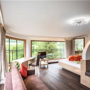 Ein modernes Wohnzimmer mit großen Fenstern und natürlichem Licht. Der Raum ist gemütlich eingerichtet mit einem Sofa, einem Tisch und dekorativen Elementen.