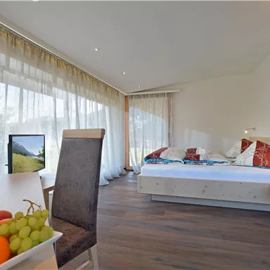 Ein gemütliches Zimmer mit großen Fenstern und hellem Licht. Auf dem Tisch liegt eine Obstschale mit verschiedenen Früchten.