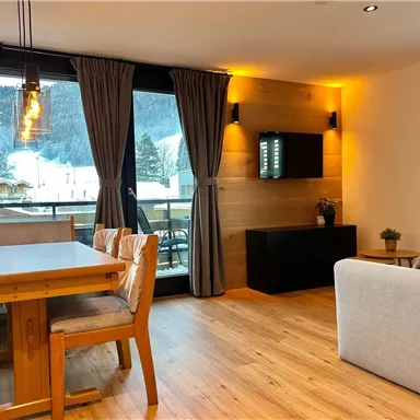 Ein modernes Wohnzimmer mit einem Essbereich und einer Wohnlandschaft. Große Fenster bieten einen schönen Blick auf die Berge.