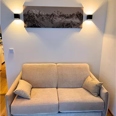 A bright living room with a beige sofa and two decorative pillows. Above the sofa hangs a black-and-white landscape picture.