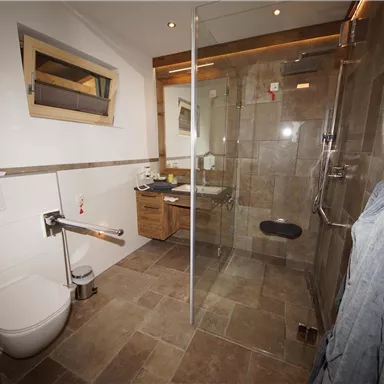 Ein modernes Badezimmer mit einer begehbaren Dusche und einer Toilette. Hell geflieste Wände und warme Holzakzente sorgen für ein einladendes Ambiente.