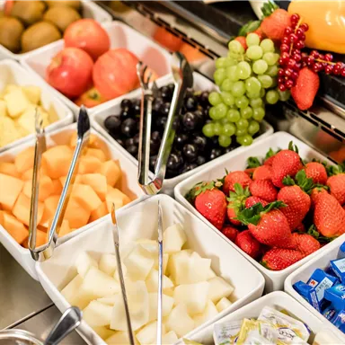 Ein frisches Obstbuffet mit verschiedenen Früchten wie Trauben, Äpfeln, Erdbeeren und Melonen. Die Früchte sind in kleinen Schalen angeordnet und laden zum Kosten ein.