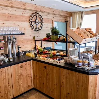Ein einladender Verkaufsstand aus Holz mit einer Auswahl an frischen Früchten, Brötchen und Getränken. Im Hintergrund befindet sich eine Kaffeemaschine und eine Uhr an der Wand.
