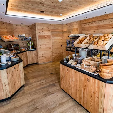 Ein gemütliches Café mit Holzinterieur und verschiedenen Backwaren. Auf den Tischen sind frische Brötchen und eine Auswahl an Snacks angerichtet.