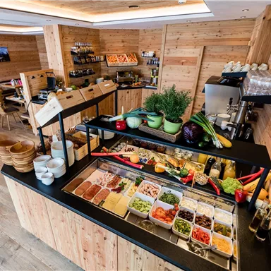 Ein einladendes Buffet mit frischem Gemüse, Aufschnitt und verschiedenen Beilagen. Der Raum hat eine gemütliche Holzverkleidung und eine freundliche Atmosphäre.