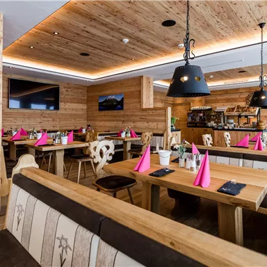 Ein gemütliches Restaurant mit Holzmöbeln und warmem Ambiente. Tischdekoration in Rosa und eine gut ausgestattete Bar sind sichtbar.