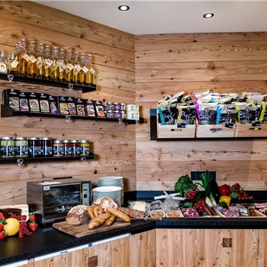 Ein gemütliches Café mit einem Holzinterieur. Auf der Theke sind frisches Obst, Brot und verschiedene Getränke zu sehen.