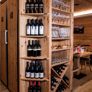 Ein eleganter Weinschrank aus Holz mit verschiedenen Flaschen Rotwein und Gläsern. Der Schrank ist gut organisiert und passt in eine gemütliche Restaurantumgebung.