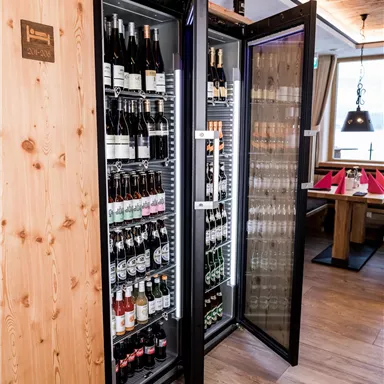 Ein eleganter Getränkekühlschrank mit verschiedenen Weinen und Bieren. Der Kühlschrank steht in einem stilvollen Restaurant mit holzverkleideten Wänden.