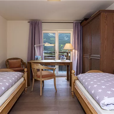 Ein gemütliches Schlafzimmer mit zwei Einzelbetten und einem Schreibtisch. Der Raum hat eine große Fensterfront, die einen Blick auf die Berge bietet.