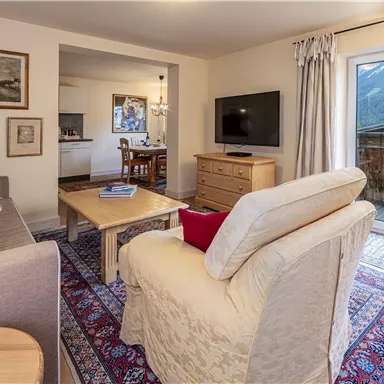 Ein gemütlicher Wohnbereich mit einem hellen Sofa, einem Tisch und einem Fernseher. Große Fenster bieten einen schönen Blick nach draußen.