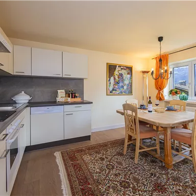 Eine helle und moderne Küche mit einem Essbereich. Der Tisch ist aus Holz und die Wände sind mit orangefarbener Dekoration verziert.