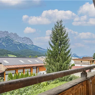 Ein malerischer Blick auf die Berge mit einer Kirche im Vordergrund. Der Himmel ist klar und die Umgebung ist grün und einladend.