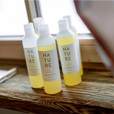 Eine Reihe von Flaschen mit Shampoo auf einem Holztisch. Die Flaschen sind mit dem Wort "NATURE" beschriftet und haben verschiedene Farben.