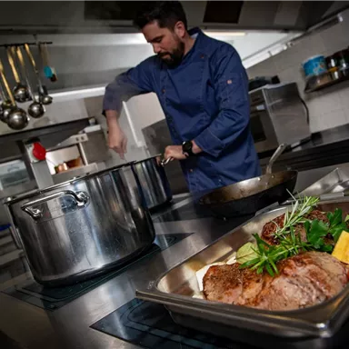 Ein Koch bereitet in einer modernen Küche ein köstliches Gericht zu. Auf der Arbeitsfläche liegt eine Platte mit Fleisch und frischem Gemüse.