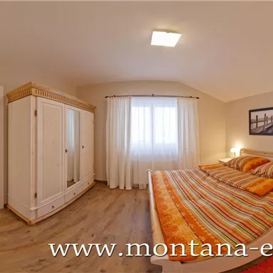 Ein gemütliches Schlafzimmer mit einem großen Doppelbett und bunten Bettdecken. Der Raum hat helle Wände und einen Fensterblick, der natürliches Licht hereinlässt.