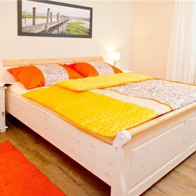 Ein gemütliches Schlafzimmer mit einem großen Bett und bunten Bettdecken. Angenehme Beleuchtung und Holzfußboden schaffen eine einladende Atmosphäre.