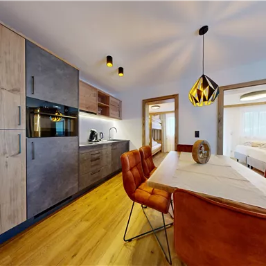 A modern kitchen with wooden cabinets and an elegant table with sleek chairs. The atmosphere is bright and inviting, perfect for social gatherings.