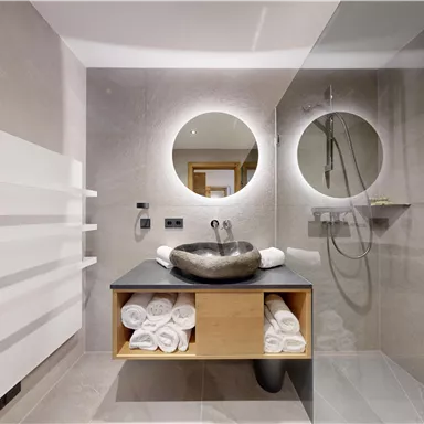 A modern bathroom with an elegant wash basin and round mirrors. Towels are neatly arranged on a shelf.