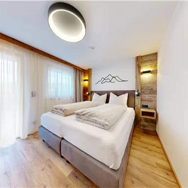 A modern bedroom with a double bed and bright curtains. The warm wood paneling and soft lighting create a cozy atmosphere.