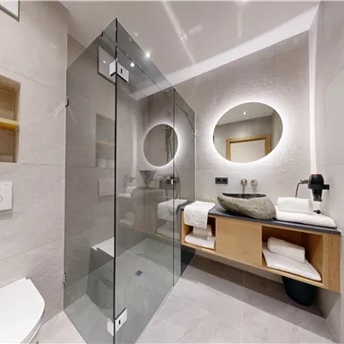A modern bathroom with a glass shower and stylish wooden shelves. The space is bright and designed in a minimalist style.